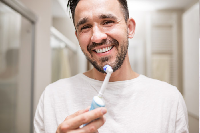 Happy dental patient using an electric toothbrush like the Oral-B Genius offered by AKJ Dentistry in Lubbock, Texas.